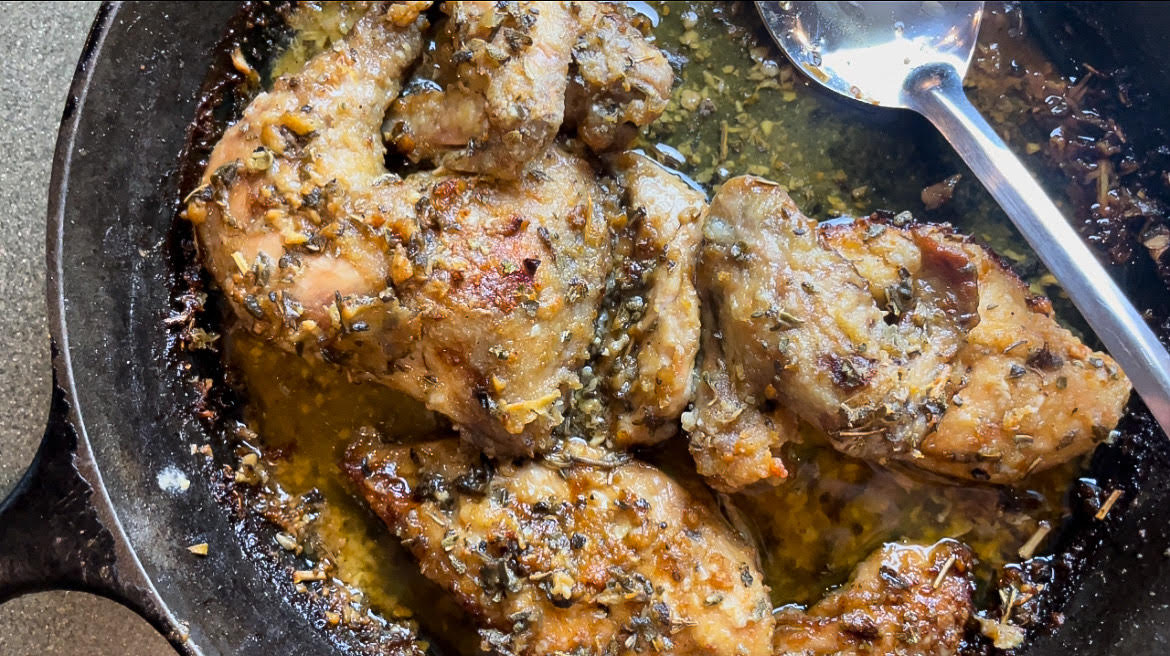 chicken fresh out of the oven in a cast iron pan with a metal ladle 