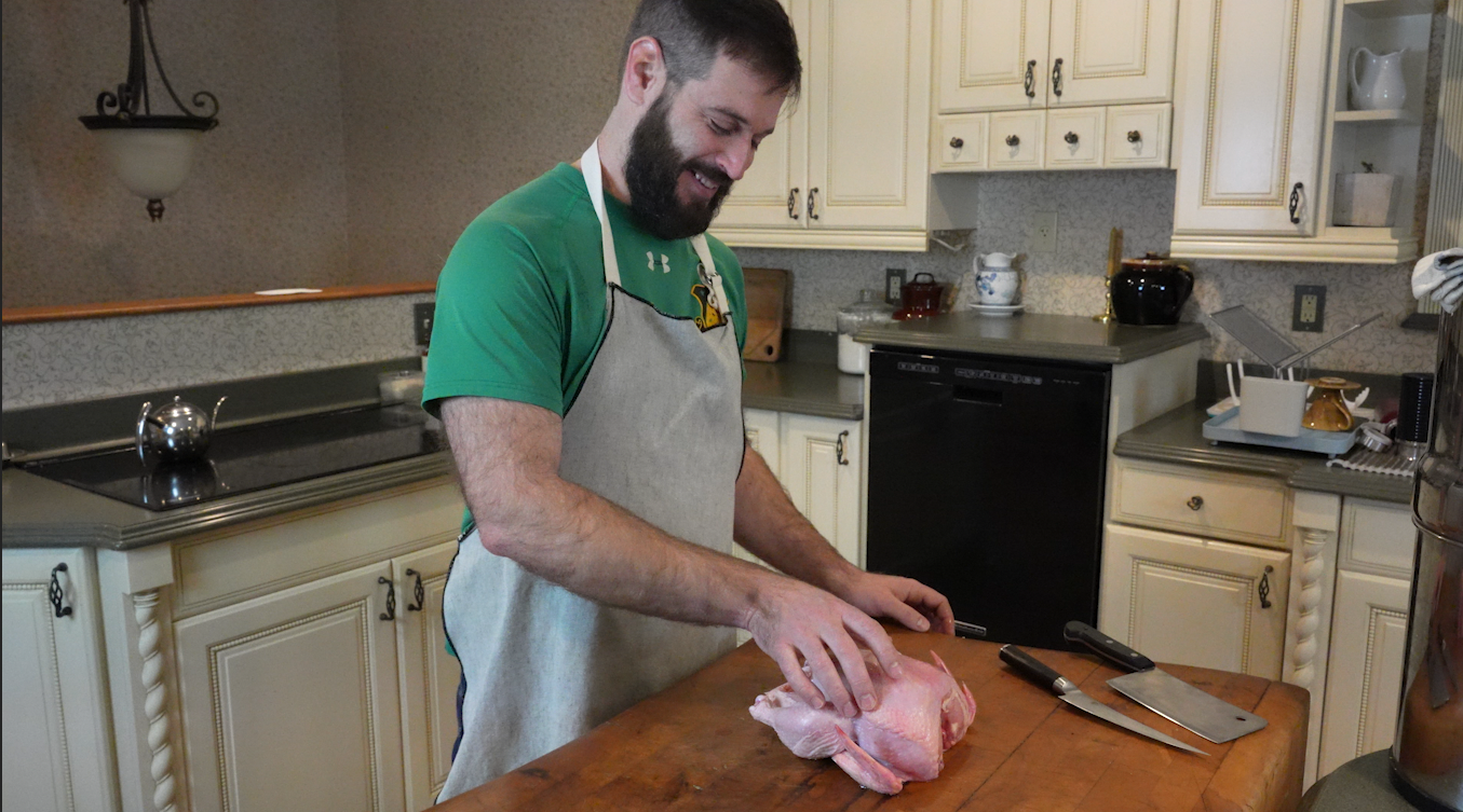 andrew cutting up a whole chicken on a butcher block. 